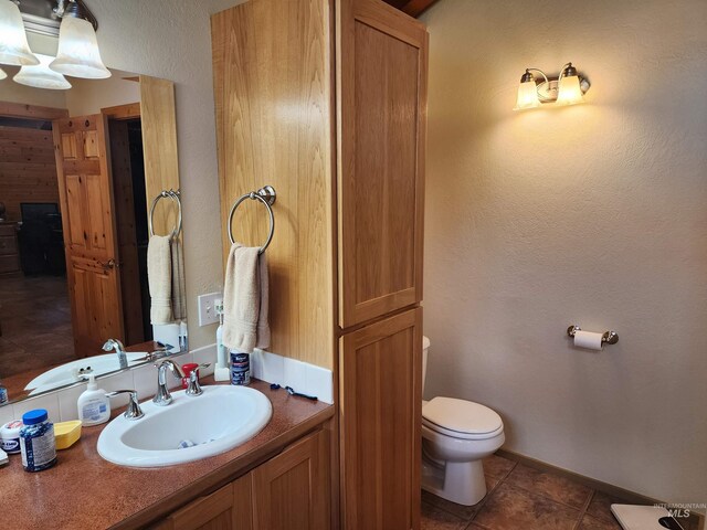 bathroom featuring a textured wall, vanity, toilet, tile patterned floors, and baseboards