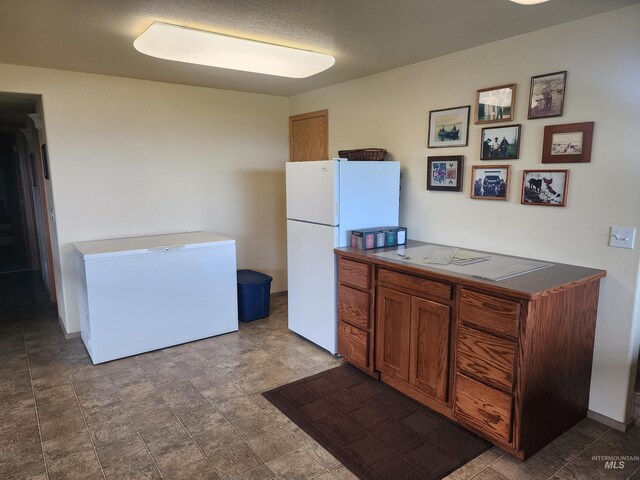 kitchen featuring dark countertops, brown cabinets, freestanding refrigerator, and refrigerator