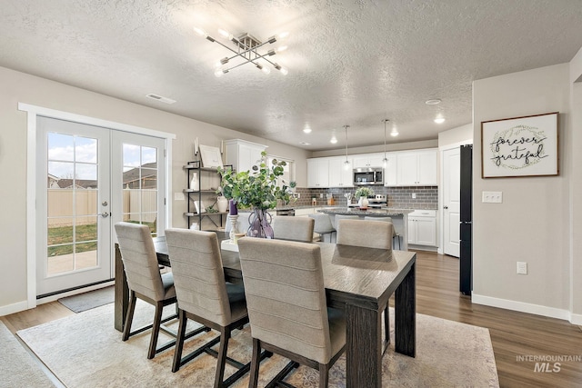 dining space with wood-type flooring, a textured ceiling, an inviting chandelier, and french doors