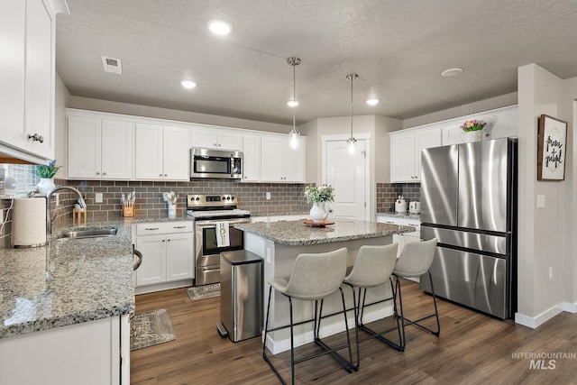 kitchen with appliances with stainless steel finishes, dark wood-type flooring, sink, a center island, and white cabinetry