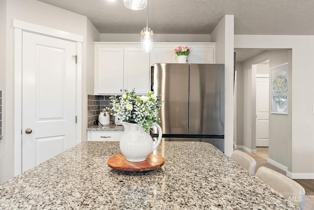 kitchen with decorative backsplash, stainless steel fridge, light stone counters, light hardwood / wood-style flooring, and white cabinetry