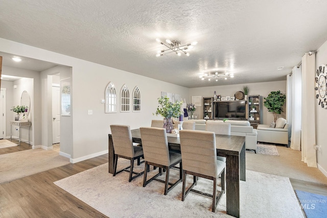 dining room featuring light wood-type flooring, a textured ceiling, and an inviting chandelier