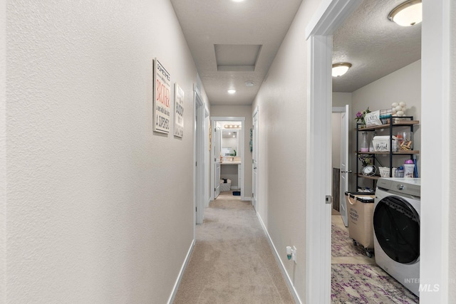 corridor featuring washer / clothes dryer, light carpet, and a textured ceiling