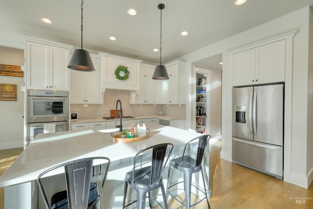 kitchen featuring an island with sink, hanging light fixtures, white cabinets, and stainless steel appliances