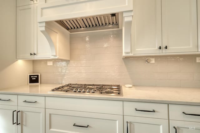 kitchen featuring backsplash, white cabinets, wall chimney range hood, and stainless steel gas cooktop