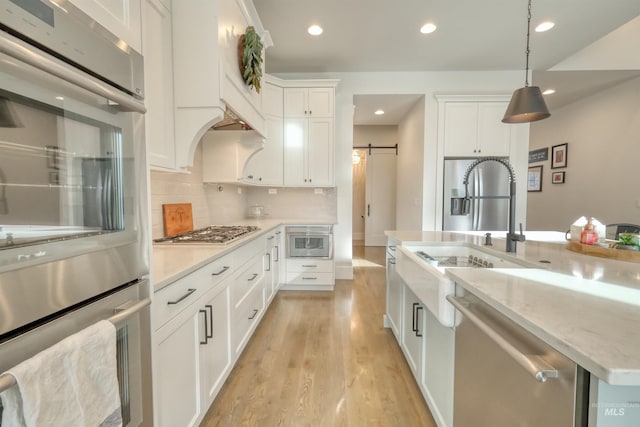 kitchen featuring stainless steel appliances, sink, a barn door, white cabinets, and hanging light fixtures