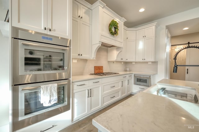 kitchen with stainless steel appliances, tasteful backsplash, light stone counters, light hardwood / wood-style flooring, and white cabinets