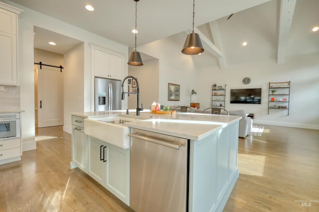 kitchen featuring a kitchen island with sink, white cabinets, hanging light fixtures, a barn door, and appliances with stainless steel finishes