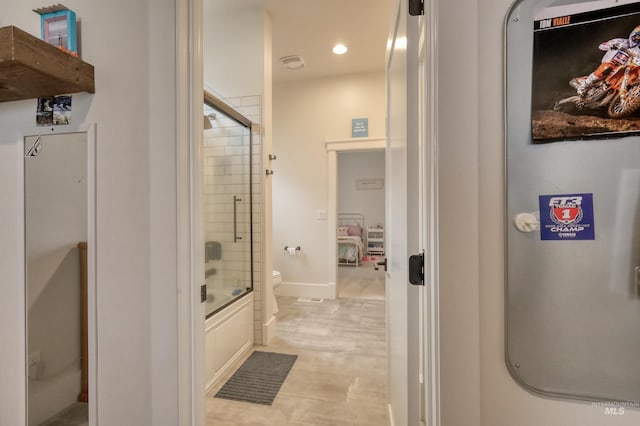 bathroom featuring toilet and shower / bath combination with glass door