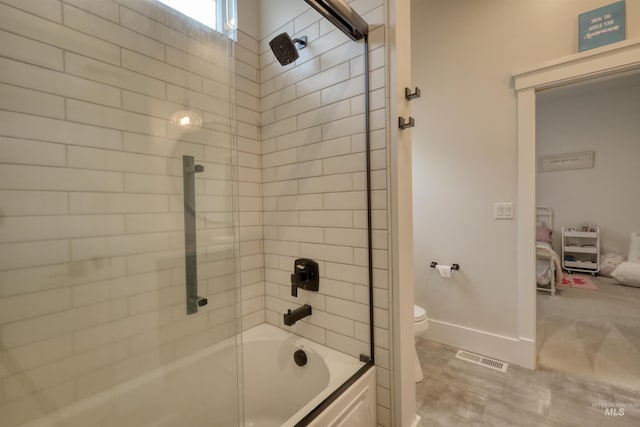 bathroom featuring toilet and bath / shower combo with glass door