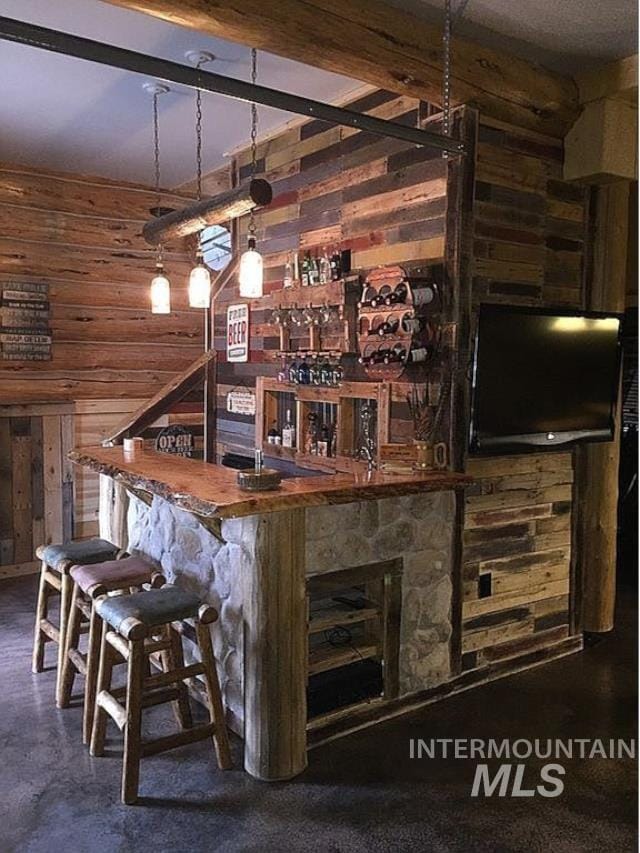 bar featuring pendant lighting, beamed ceiling, and wood walls