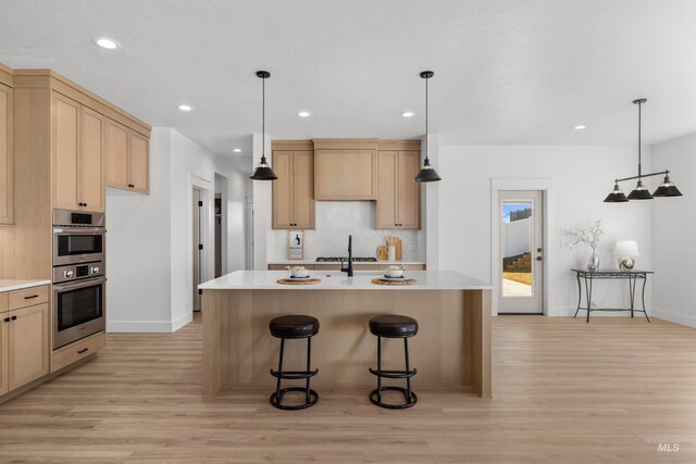 5687 S Snowden Ave, Meridian, ID 83642 - kitchen with light brown cabinetry, double oven, a breakfast bar area, light countertops, and light wood-style floors