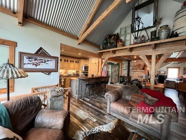 living room featuring vaulted ceiling with beams, hardwood / wood-style flooring, and a wood stove