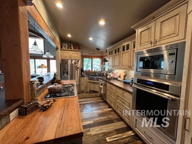 kitchen featuring appliances with stainless steel finishes, vaulted ceiling, cream cabinetry, butcher block countertops, and dark wood-type flooring