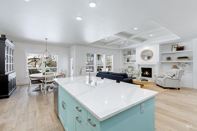 kitchen featuring coffered ceiling, sink, light wood-type flooring, a wealth of natural light, and a kitchen island with sink