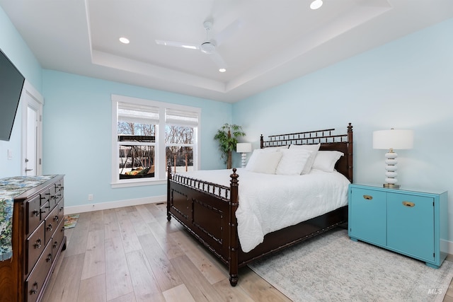 bedroom with ceiling fan, a tray ceiling, and light wood-type flooring