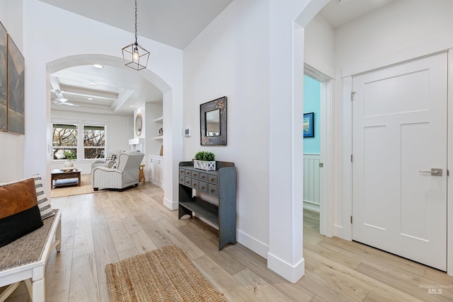 hall with built in shelves, a raised ceiling, and light wood-type flooring