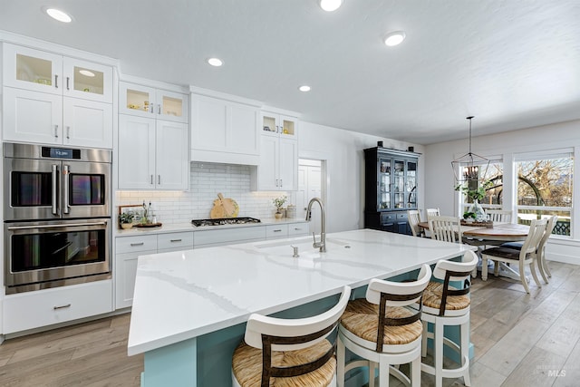 kitchen featuring hanging light fixtures, an island with sink, stainless steel double oven, and white gas stovetop