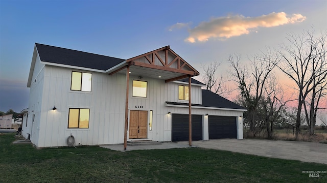 back house at dusk featuring a garage and a lawn