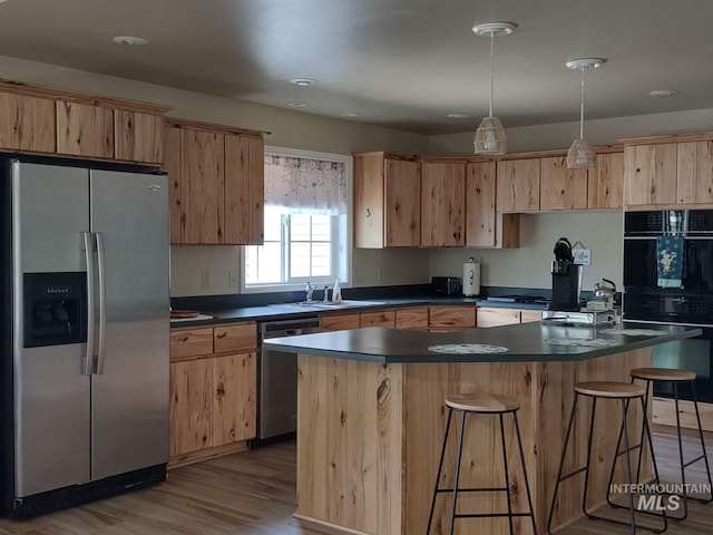 kitchen with a center island, hanging light fixtures, light wood-type flooring, light brown cabinets, and stainless steel appliances