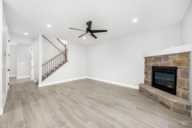 unfurnished living room with ceiling fan, light wood-type flooring, and a stone fireplace