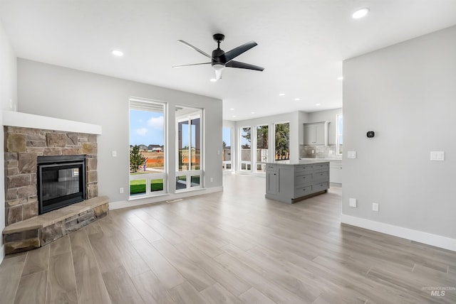 unfurnished living room featuring light hardwood / wood-style flooring, ceiling fan, and a stone fireplace