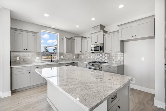 kitchen featuring stainless steel appliances, light stone counters, backsplash, a kitchen island, and sink