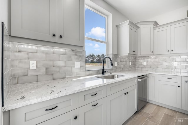 kitchen with sink, backsplash, stainless steel dishwasher, and light stone counters