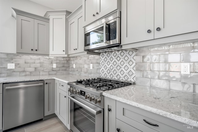 kitchen with decorative backsplash, appliances with stainless steel finishes, gray cabinetry, and light stone counters