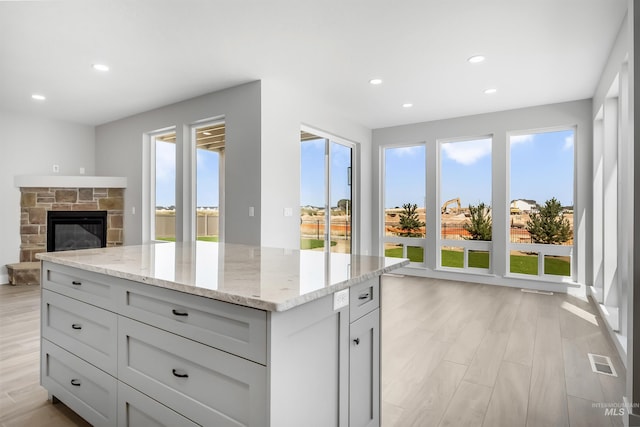 kitchen featuring a center island, light stone countertops, light wood-type flooring, and a fireplace