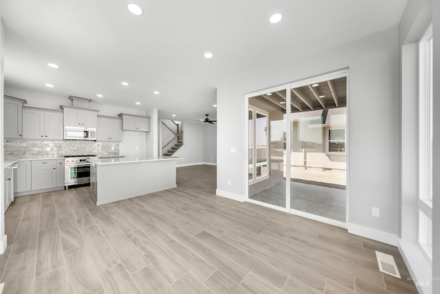 kitchen with stainless steel range oven, ceiling fan, light hardwood / wood-style floors, decorative backsplash, and a kitchen island