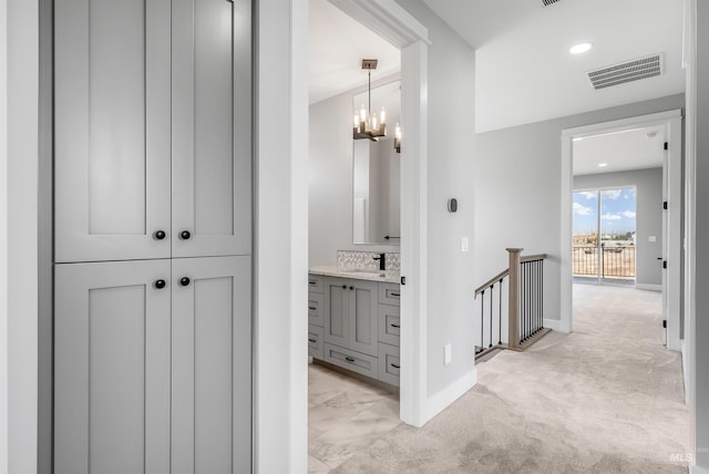 corridor with an inviting chandelier, sink, and light colored carpet