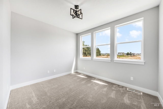 carpeted spare room featuring a chandelier