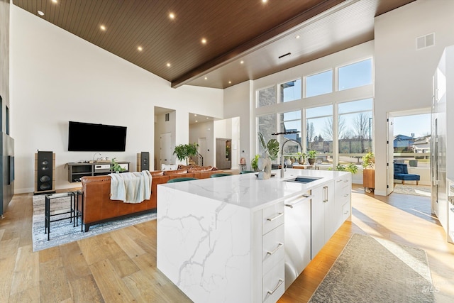 kitchen featuring light stone countertops, white cabinetry, an island with sink, sink, and wooden ceiling