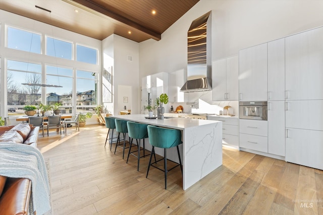 kitchen featuring beamed ceiling, light hardwood / wood-style flooring, stainless steel oven, white cabinets, and wooden ceiling