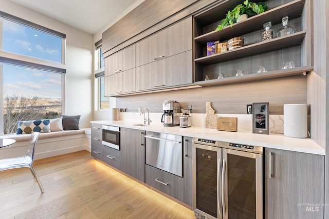 bar featuring beverage cooler, light hardwood / wood-style floors, sink, stainless steel microwave, and gray cabinetry