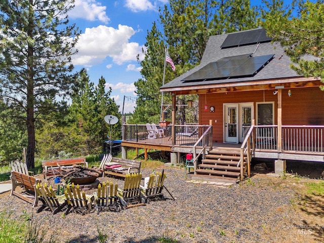 10389 Gamann Dr, Cascade, ID 83611 - back of house with roof mounted solar panels, a shingled roof, an outdoor fire pit, and a deck