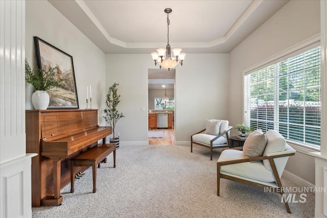sitting room with light colored carpet, a chandelier, a raised ceiling, and baseboards