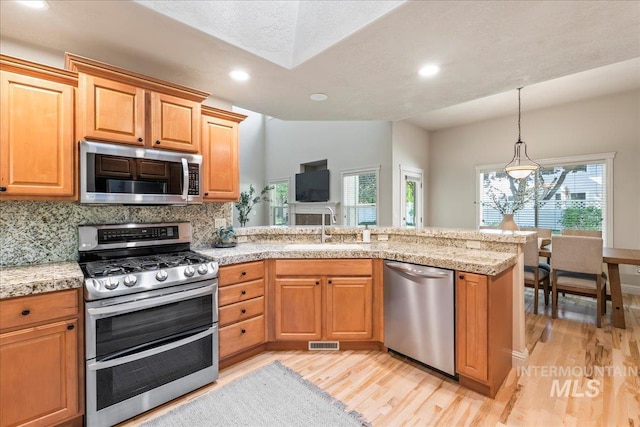 kitchen with appliances with stainless steel finishes, a sink, a peninsula, light wood-style floors, and recessed lighting