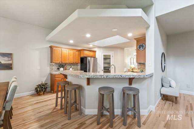 kitchen with freestanding refrigerator, a breakfast bar, light wood-type flooring, and recessed lighting