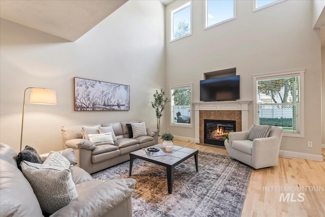 living area with a high ceiling, baseboards, a tile fireplace, and plenty of natural light