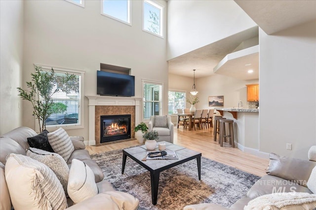 living area with a towering ceiling, plenty of natural light, light wood finished floors, a tile fireplace, and baseboards