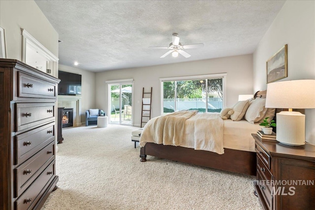 bedroom with access to exterior, light carpet, a glass covered fireplace, and a textured ceiling