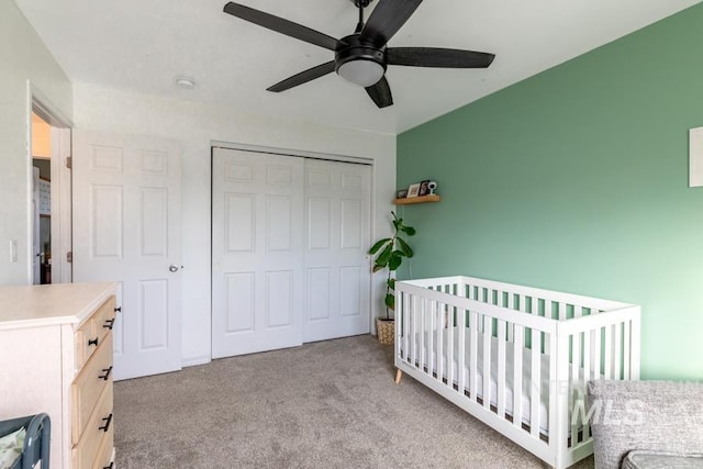 carpeted bedroom with a crib, a closet, and ceiling fan