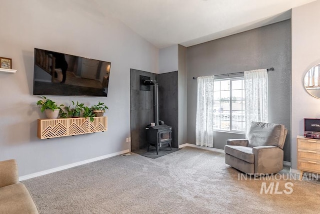 sitting room featuring vaulted ceiling, a wood stove, baseboards, and carpet floors