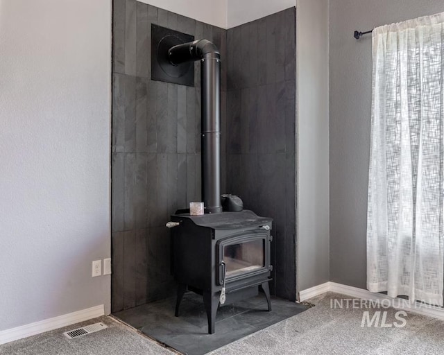 interior details featuring visible vents, a wood stove, baseboards, and carpet floors