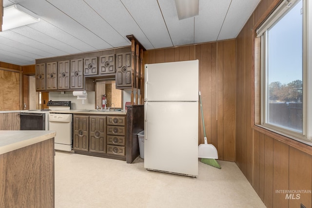 kitchen with white appliances, light colored carpet, wooden walls, and sink