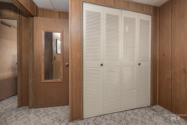 hall featuring wooden walls, a textured ceiling, and light colored carpet