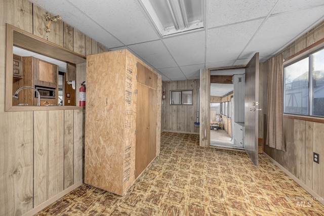 hallway with a paneled ceiling, wooden walls, and sink