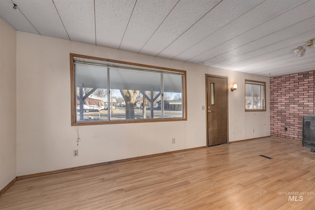 unfurnished living room with brick wall, light wood-type flooring, and a wood stove